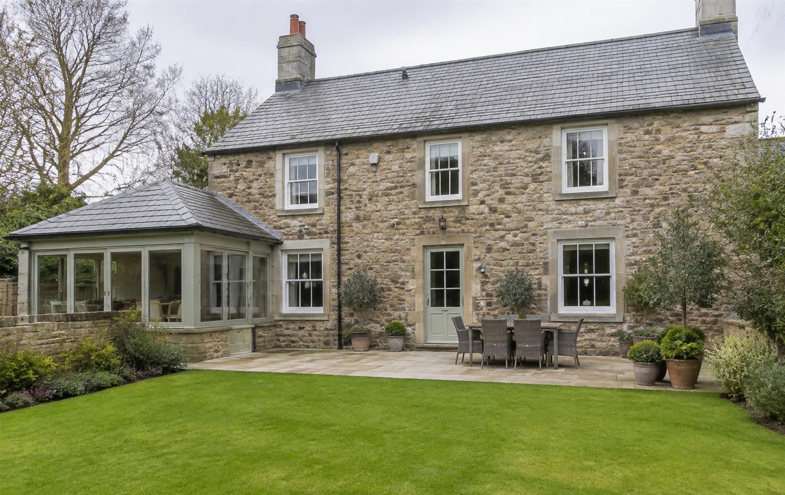 The rear of a British stone house with painted sash windows and a patio